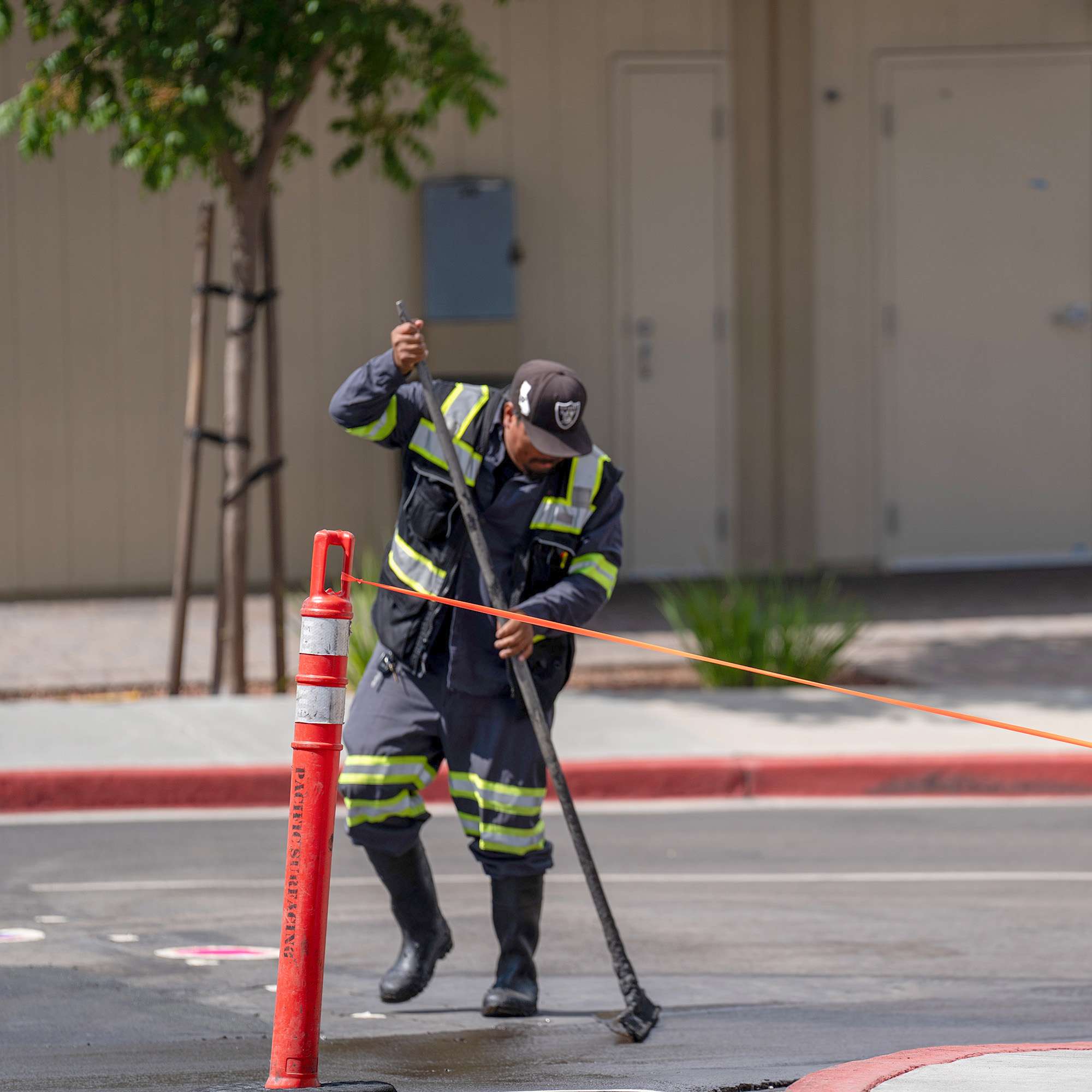 Pacific Surfacing team member applying sealcoat near a curb behind safety cones.
