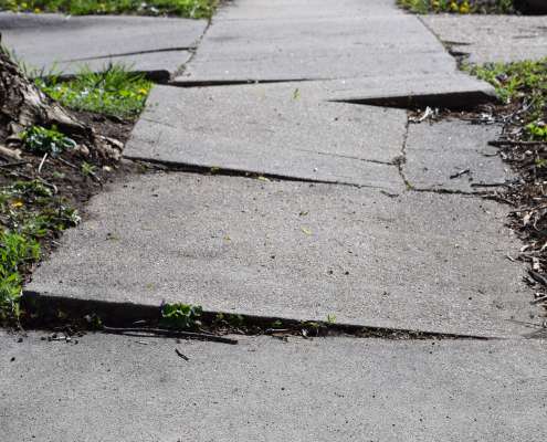 Lifted and cracked concrete sidewalk with a significant trip hazard.