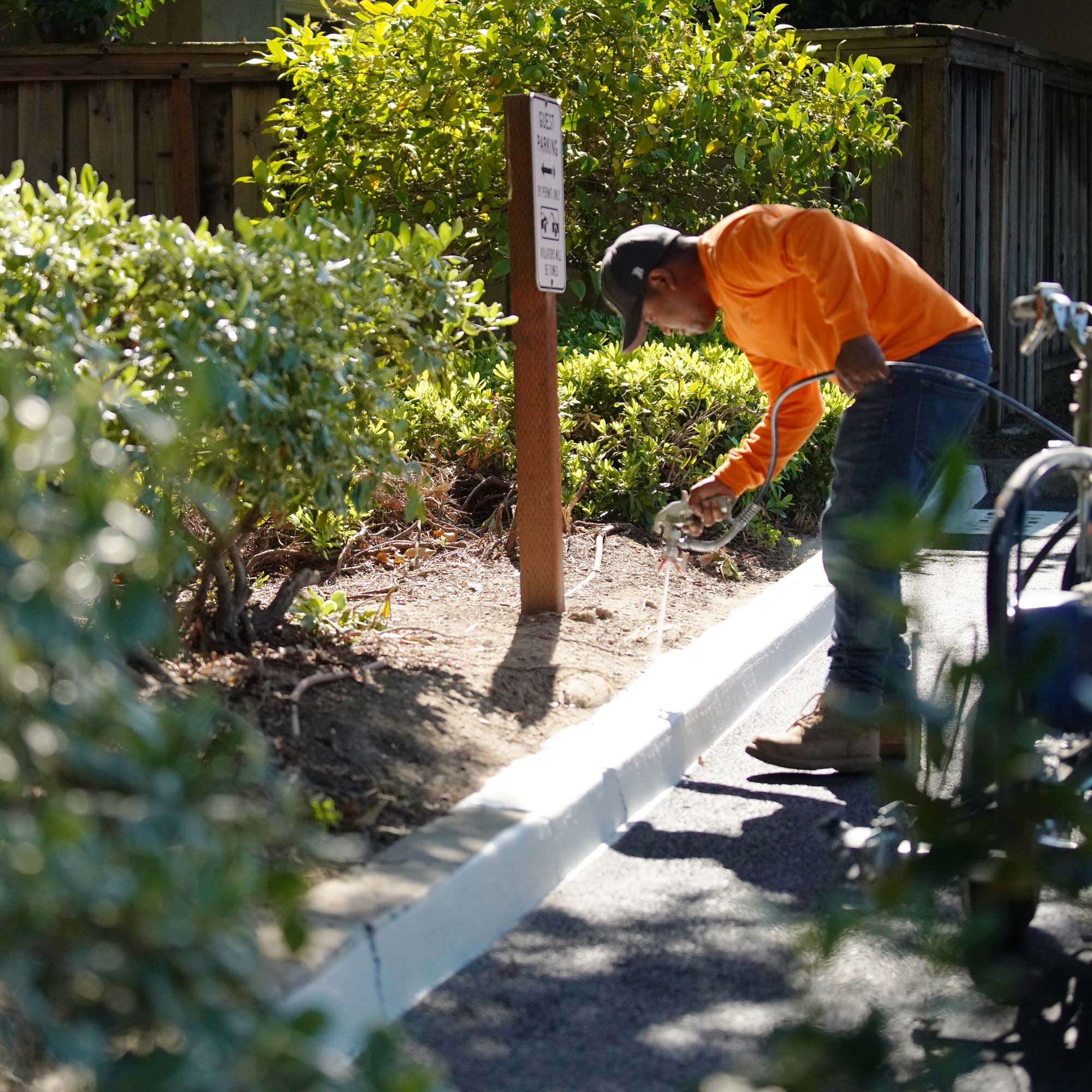 Pacific Surfacing crew member applying white paint to a curb with a striping gun.